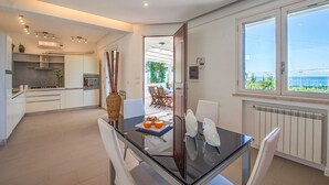 A modern kitchen with white cabinets, a dining area with a glass table, and a view of the sea through large windows. - Villa Mondello Addaura Sea View (Palermo)