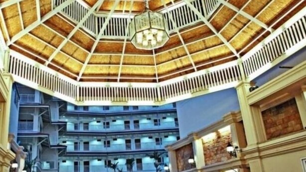 Een hotelatrium met een hoge plafond, meerdere verdiepingen en een centrale kroonluchter.