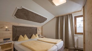 Ein Schlafzimmer mit zwei Betten, Holz-Kopfteilen, einer geneigten Decke und einem Fenster mit Vorhängen.