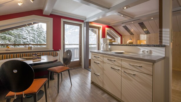 Eine moderne Küche mit integriertem Backofen, eine Essecke mit Bank und Stühlen sowie der Blick auf schneebedeckte Bäume durch das Fenster.