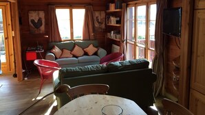 Ein gemütliches Blockhaushaus-Interieur mit einem grünen Sofa, einem roten Sessel, einem Tisch und einem Fernseher.