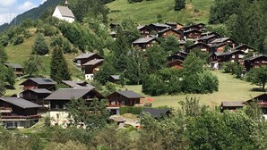 Eine Gruppe Holzhütten an einem Hügel mit einer Kirche im Hintergrund.