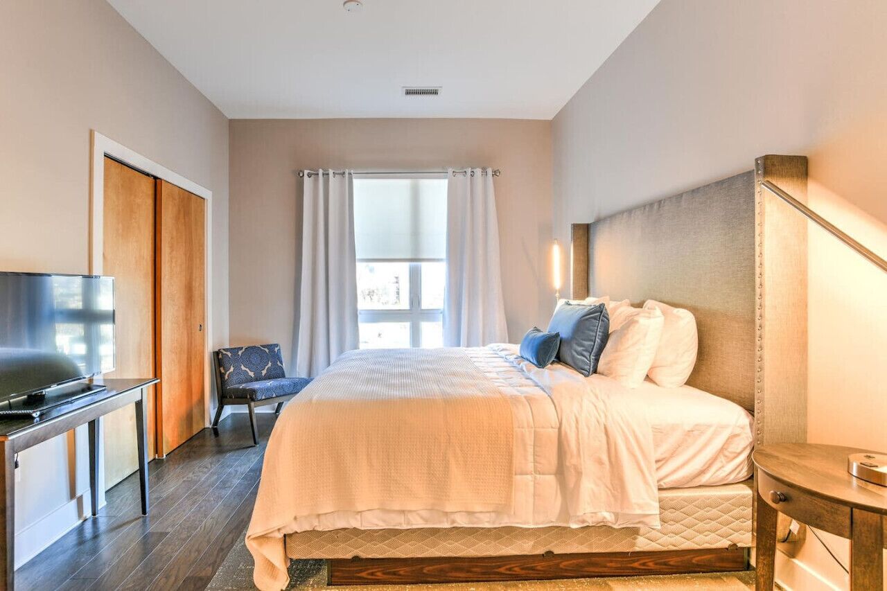 A hotel room with a bed, a TV, a chair, and a window with curtains.