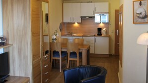A compact kitchen with white cabinets, a microwave, and a sink. There is a dining area with a table and chairs.