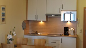 A compact kitchen with wooden cabinets, a microwave, and a coffee maker. There is a dining table with chairs and a vase with flowers.