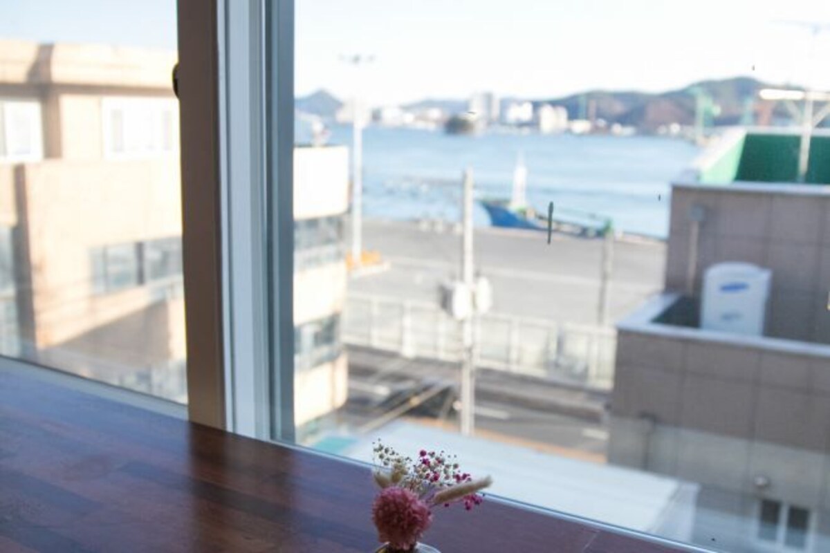 A view from a window overlooking a harbor with boats, buildings, and a clear sky.