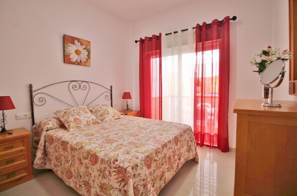 A bedroom with a bed, nightstands, a dresser, a mirror, and a window with curtains.