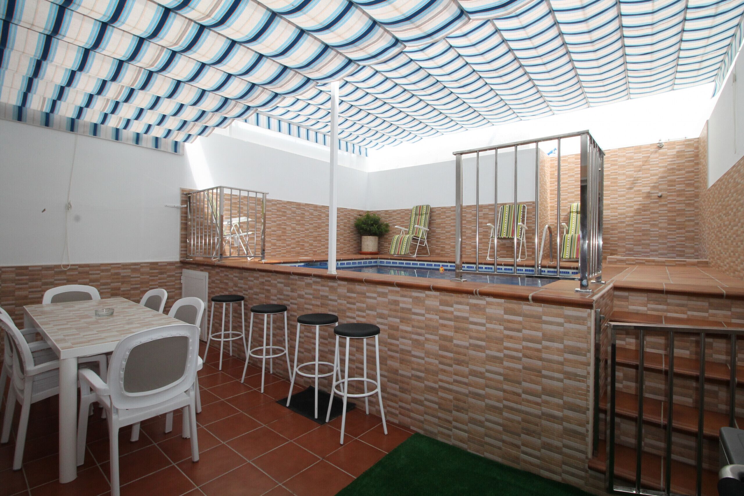 A covered outdoor dining area with a pool, white chairs, and a bar counter.