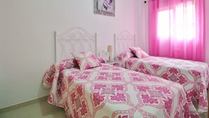 Ein Schlafzimmer mit zwei Betten, rosa Bettwäsche, einem Nachttisch, einer Lampe und einem Wandbild.