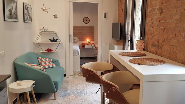 Un espacio habitable moderno con un sofá color turquesa, una mesita blanca, un escritorio blanco con individuales tejidos, y una pared de ladrillo.