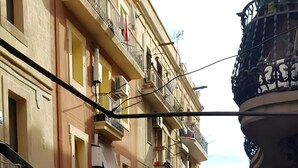 Un balcón con una bandeja de madera que contiene naranjas y limones, baranda de hierro forjado y vistas a una calle con edificios y balcones.