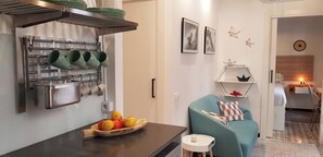 Eine moderne Küche mit Obstschale, hängenden Tassen und einem Essbereich mit einem Türkis-sofa und einem kleinen Beistelltisch.