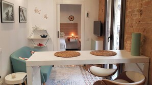 Una sala de estar moderna con una mesa blanca, un sillón verde azulado y una pequeña mesa redonda con una vela.