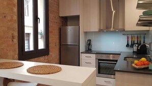 Una cocina con pared de ladrillo, un refrigerador de acero inoxidable, un horno empotrado y una ventana con vista a la calle.