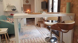 Una cocina moderna con mostrador blanco, dos taburetes de bar, un mantel tejido y una taza verde en la pared.
