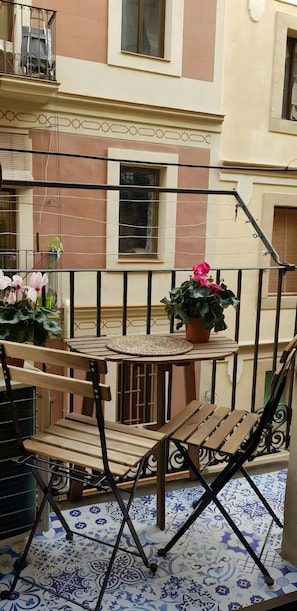 Ein Balkon mit Holztisch, Stühlen, Topfpflanzen und fugenlosen Bodenfliesen.