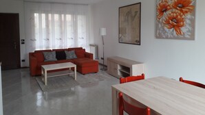 A modern living room with a red sofa, a wooden coffee table, a dining table with red chairs, and a painting of flowers on the wall.