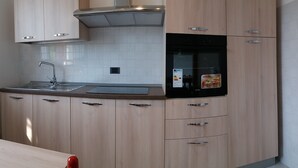 A modern kitchen with light wood cabinets, a stainless steel sink, and a black oven.