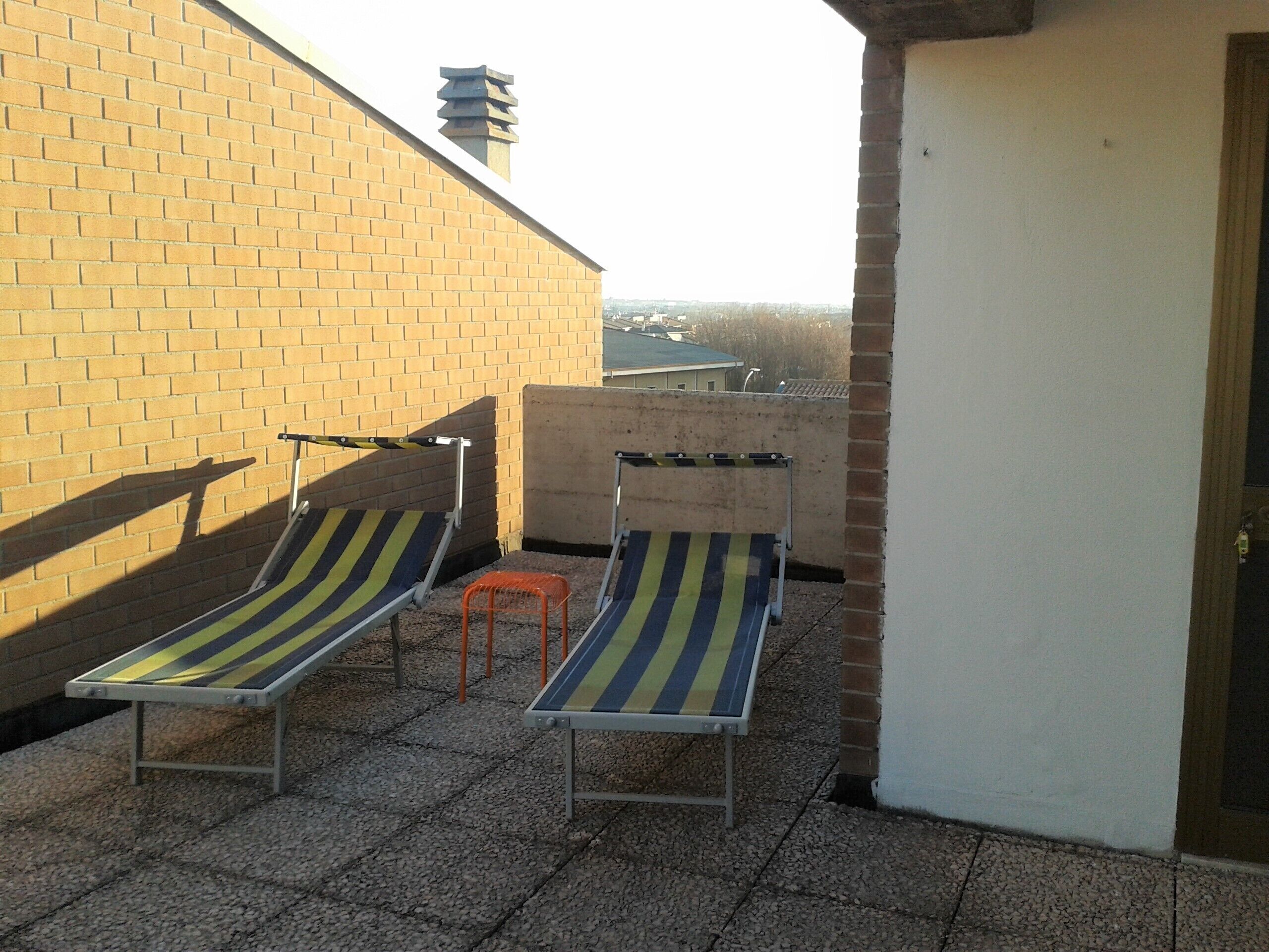 Terraza en la azotea con dos sillones de lounge y un taburete naranja.