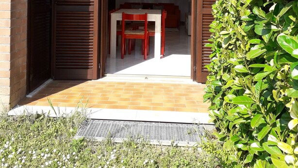 An open sliding door leading to a dining area with a table and chairs, a red pendant light, and a brick wall.
