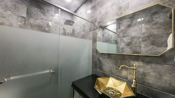 A modern bathroom with a glass-enclosed shower, a black countertop, and a gold-finished sink.