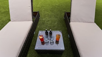 Two lounge chairs with white cushions on a rectangular table with four glasses and two bottles.