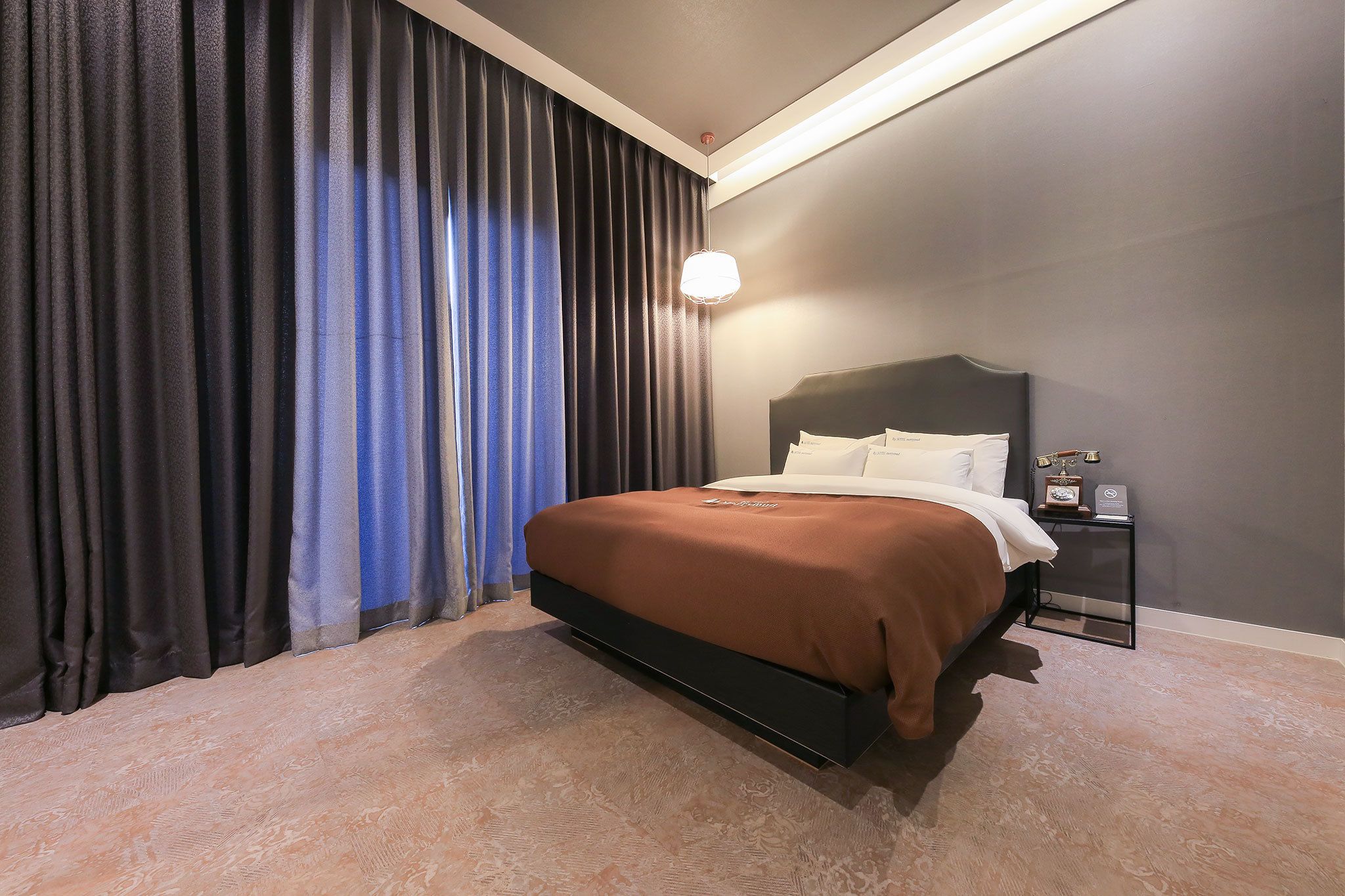 Une chambre d’hôtel avec un lit, une table de chevet et une grande fenêtre avec des rideaux.