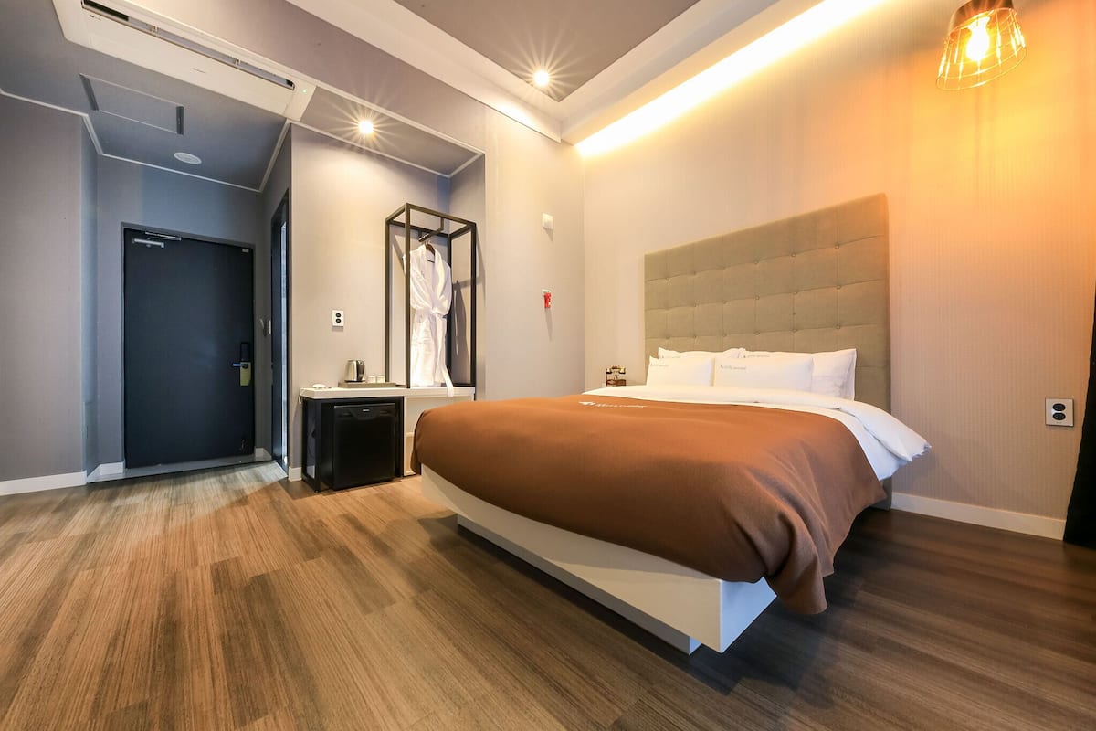 A modern hotel room with a large bed, a bedside table, a wardrobe, and a bathroom door.