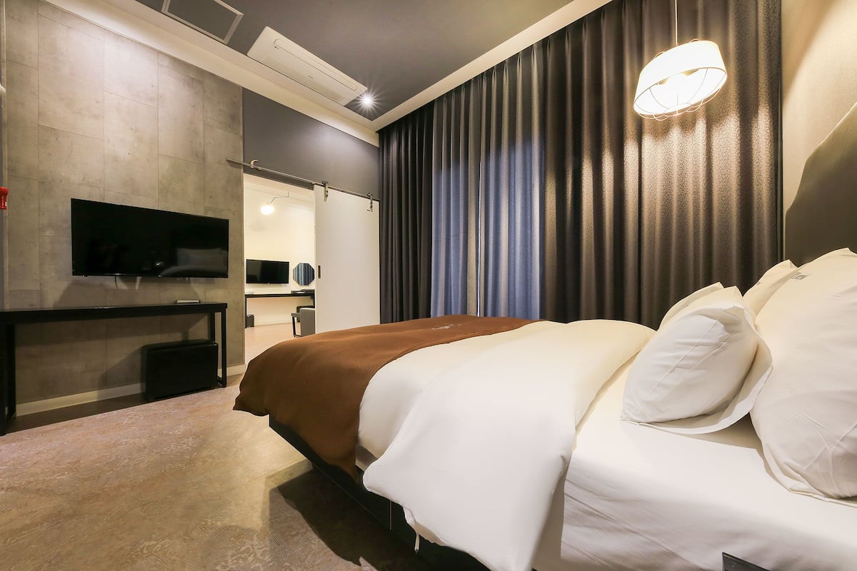 A modern hotel room with a large bed, a flat-screen TV, a desk, and a mirror.