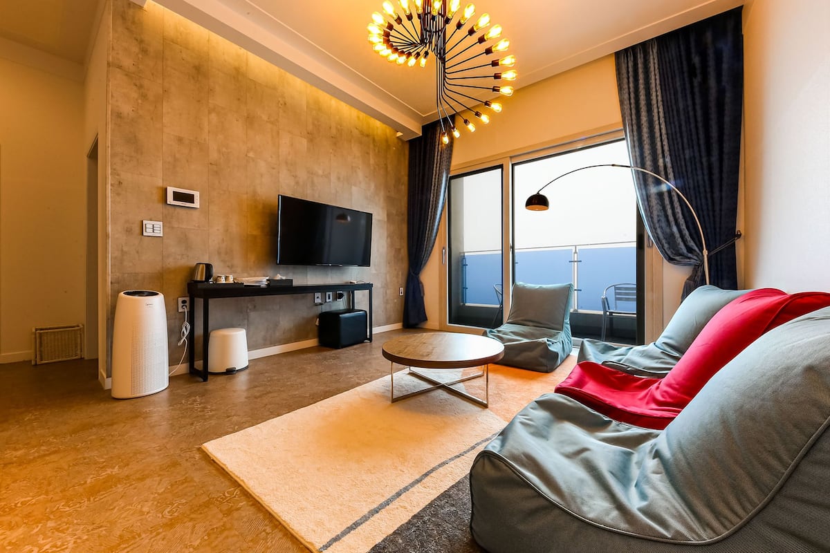 A modern living room with a flat-screen TV, a round coffee table, and a sofa with red cushions.