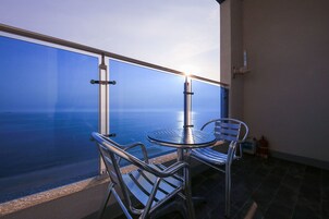 A balcony with a glass railing overlooking the sea, featuring a table and chairs.
