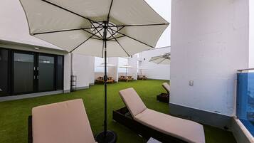 A rooftop terrace with lounge chairs, a large umbrella, and picnic tables.