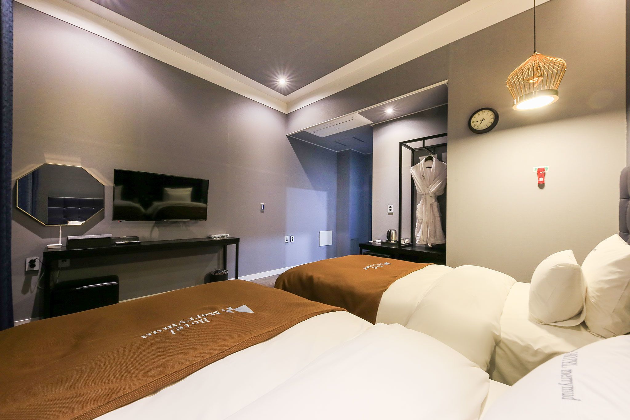 A hotel room with two beds, a TV, a desk, a mirror, and a clock on the wall.