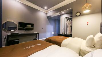 A hotel room with two beds, a TV, a desk, a mirror, and a clock on the wall.
