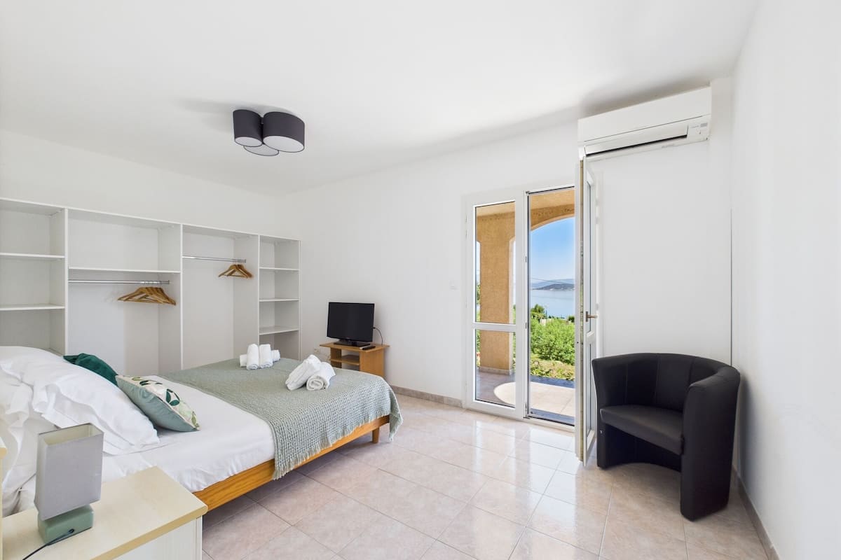 A modern bedroom with a bed, a TV, a wardrobe, and a balcony with a view.