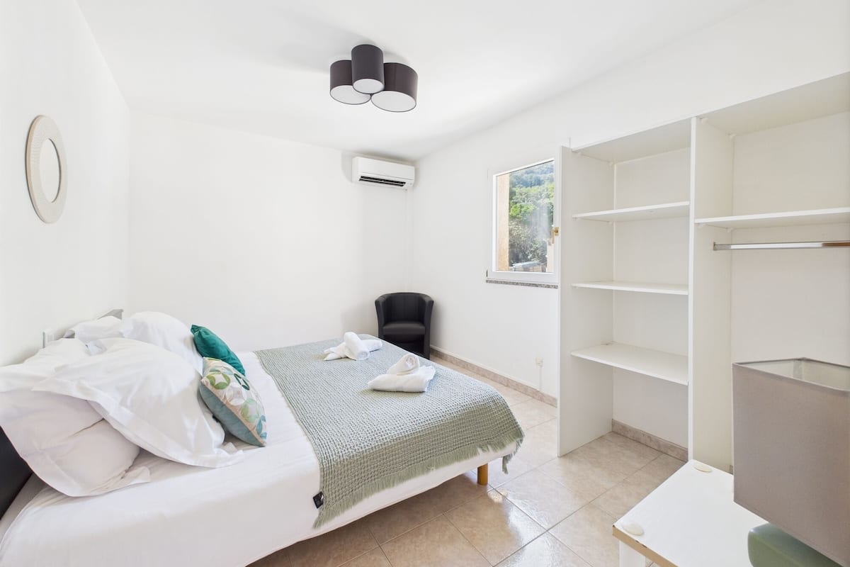 A bedroom with a bed, a chair, a wardrobe, and a window.