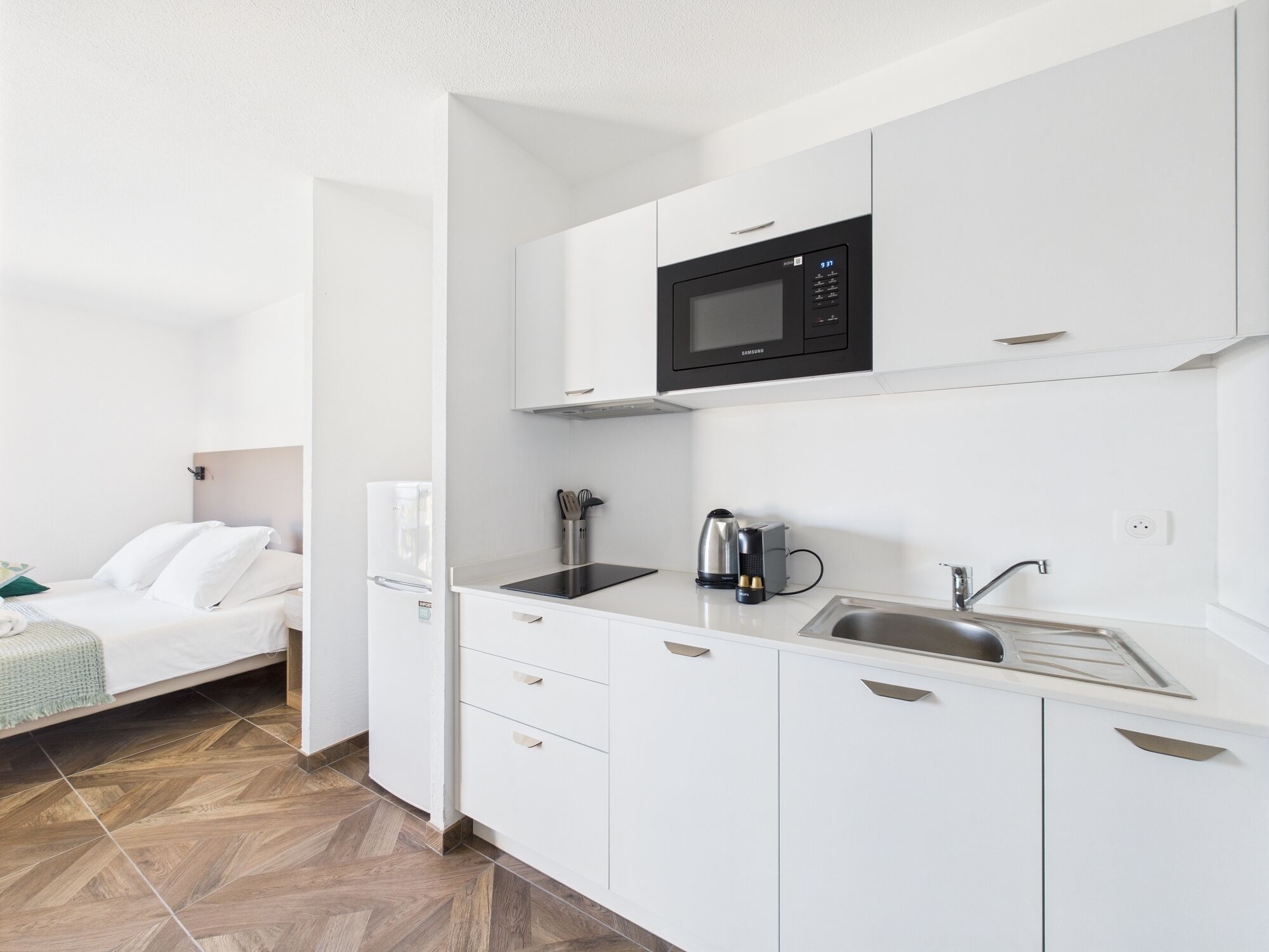 A modern kitchen with white cabinetry, a microwave, a kettle, and a sink.