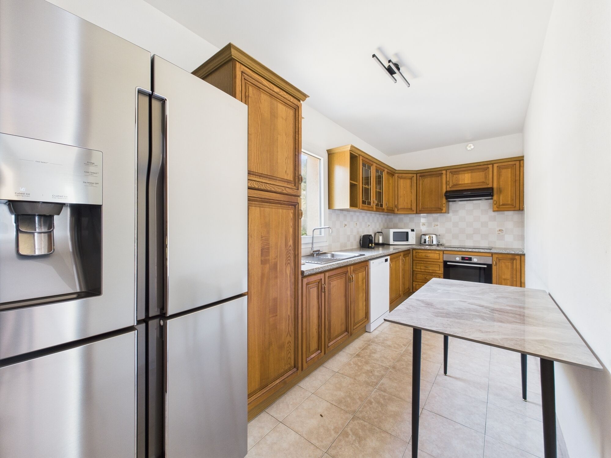 A modern kitchen with stainless steel appliances, wooden cabinets, a marble countertop, and a built-in dishwasher.