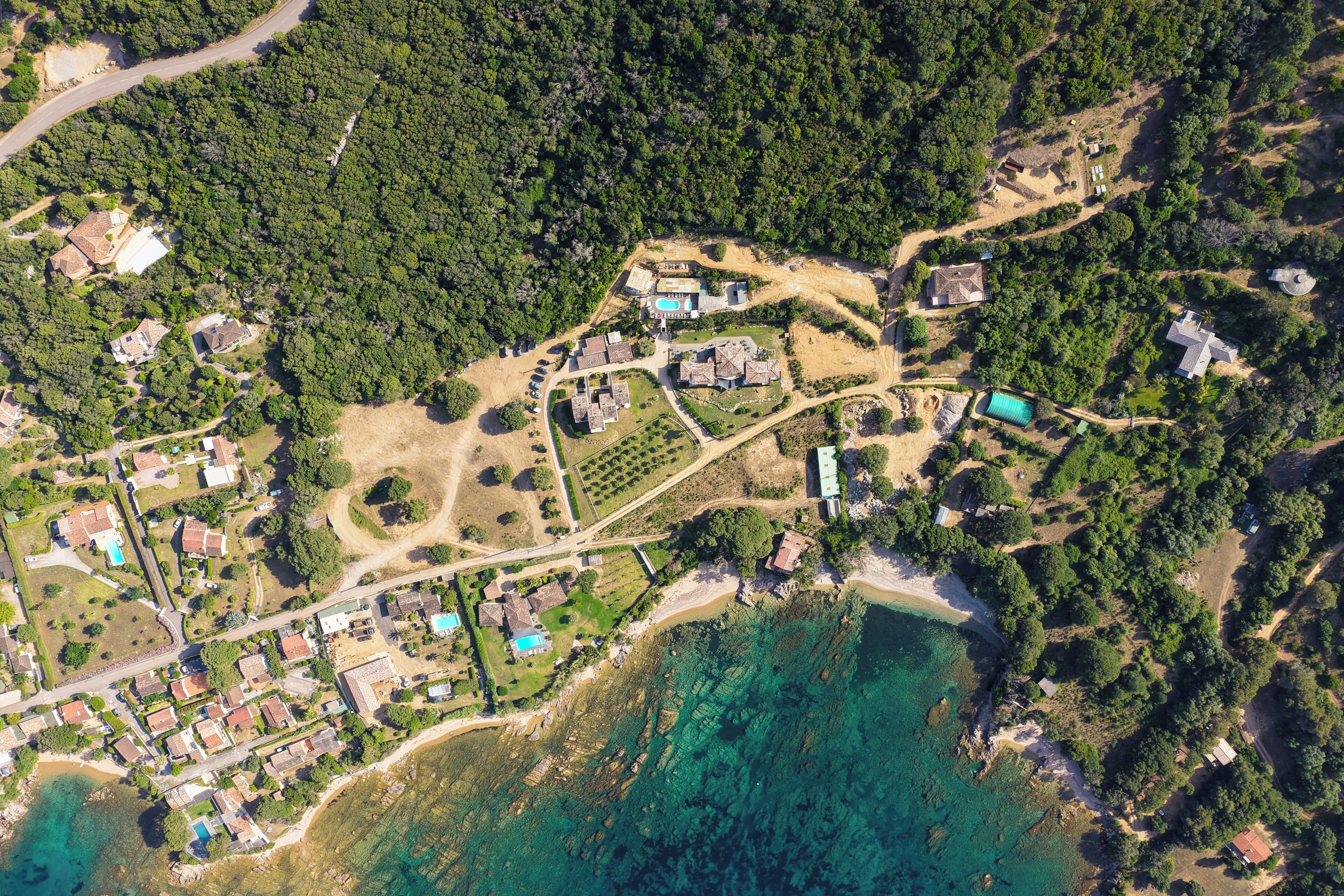 An aerial view of a coastal area with houses, a swimming pool, and a beach.