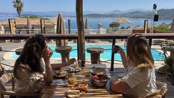 Two people dining at a table with a pool and mountains in the background.