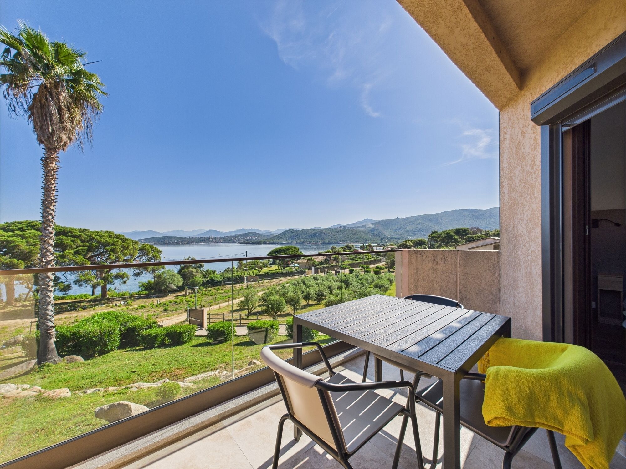 A balcony with a table and chairs, overlooking a scenic view of a lake and mountains.