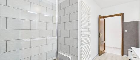 A modern bathroom with a glass shower enclosure, tiled walls, a built-in radiator, and a wooden door.