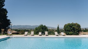 A clear blue swimming pool with four lounge chairs and a decorative chair, surrounded by greenery and a view of distant mountains. - Seventeenth-century Villa Giulia with panoramic swimming pool, +15 beds ((PERUGIA))