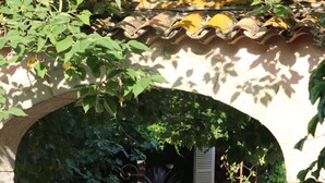 Una entrada arqueada con una reja metálica, un camino de grava y un jardín con arbustos podados y una planta en maceta.
