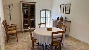 Un comedor con una mesa redonda, sillas de madera, un aparador con puertas de cristal y una pequeña encimera de cocina con adornos.