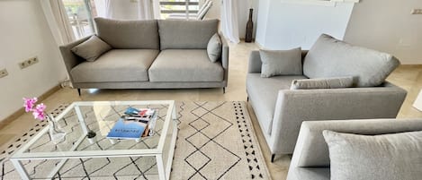 Uma sala de estar moderna com um sofá, uma mesa de centro e vista para uma varanda.