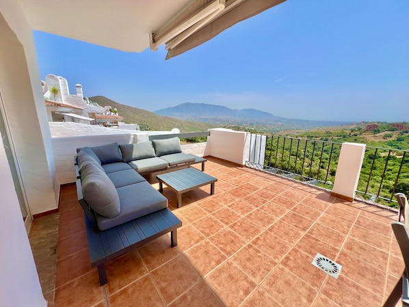 Eine Terrasse mit Sofa, Tisch, Geländer und Blick auf die Landschaft.