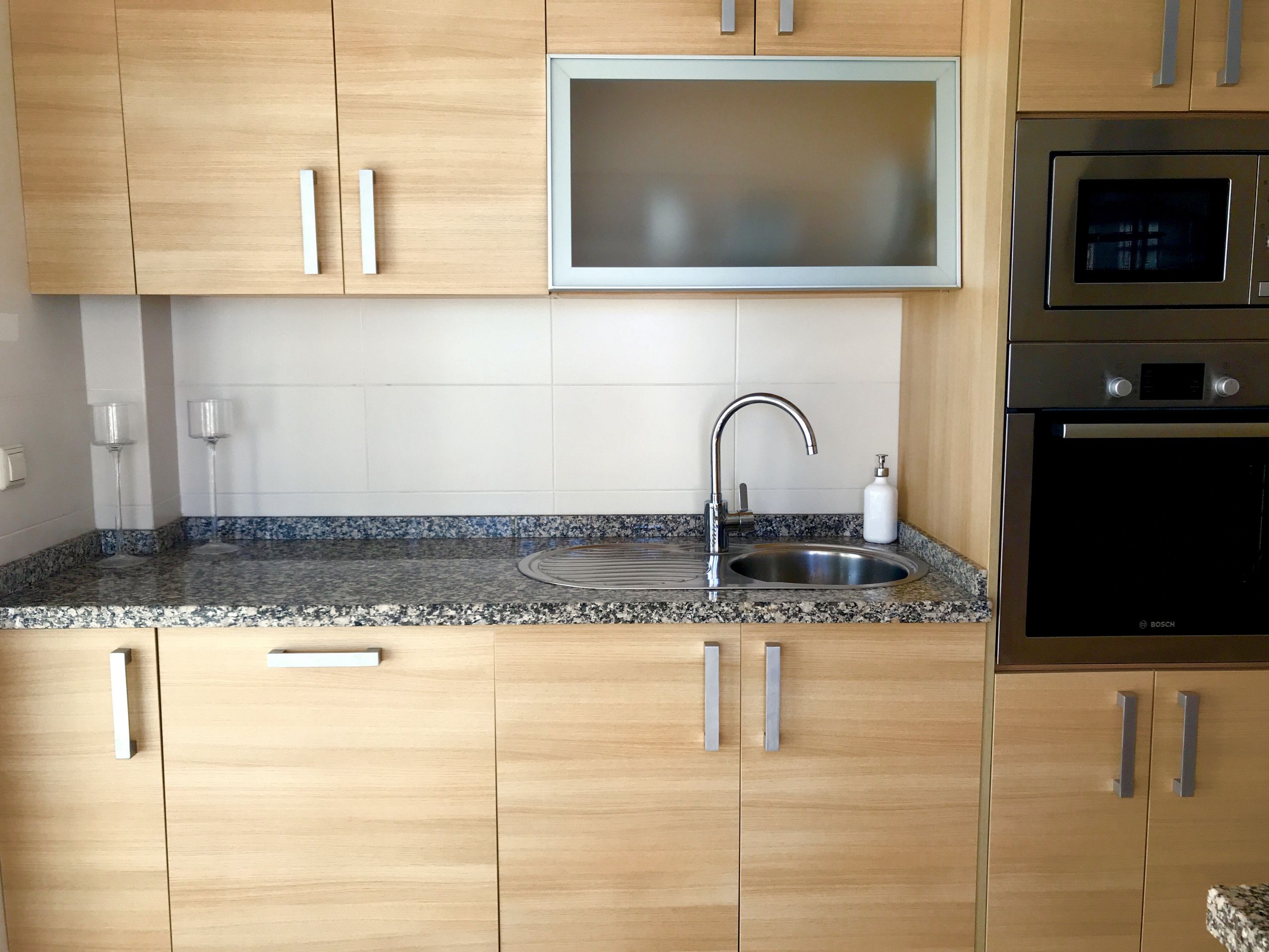 A kitchen with wooden cabinets, a stainless steel sink, a Bosch oven, and a backsplash with a speckled pattern.