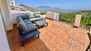 Um terraço com sofá, mesa, guarda-corpo e vista para o campo.