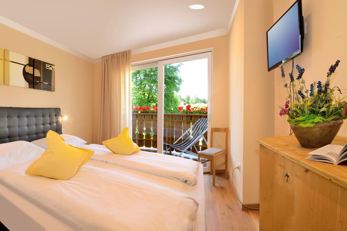 Ein Hotelzimmer mit zwei Betten, einem Fernseher, einem Schreibtisch mit Blumenvase und Blick auf einen Balkon mit einer Hängematte.